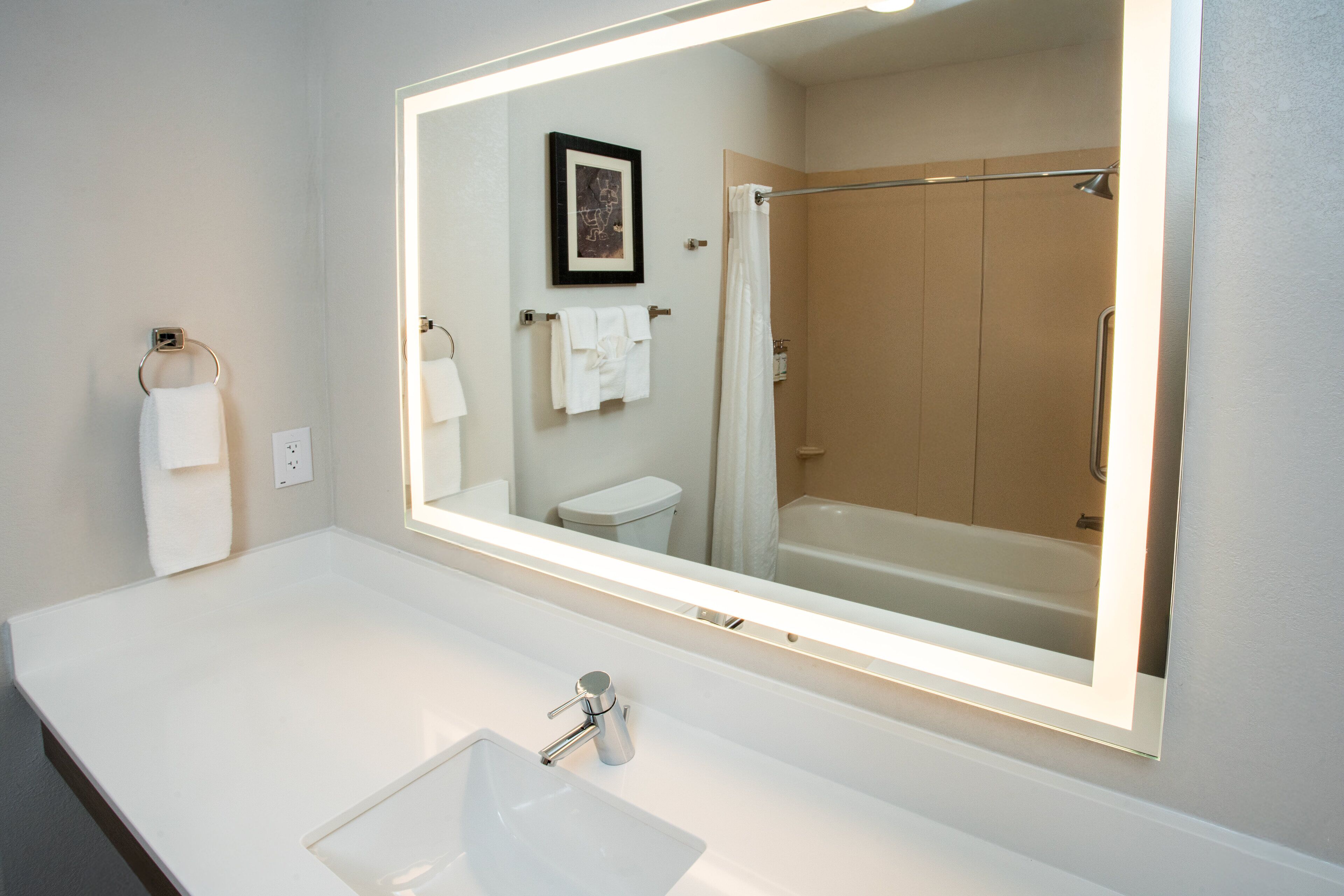 A bathroom with a large mirror, a white sink, and a shower.