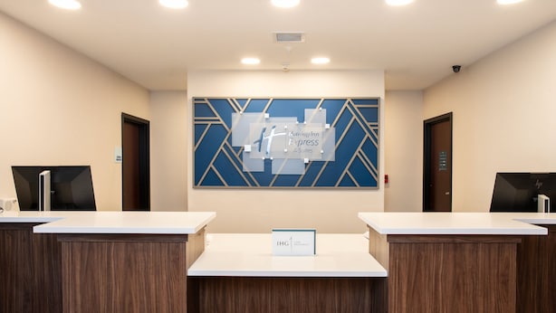 Un espace d’accueil comprenant deux comptoirs de réception, un mur décoré d’un motif géométrique bleu et une enseigne indiquant « Holiday Inn Express & Suites ».