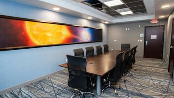 A conference room with a long table, black chairs, a large painting of a celestial scene, and a patterned carpet.