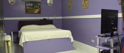 Une chambre à coucher avec un lit, une télévision et une petite étagère.
