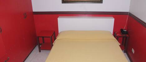 A room with a bed, a small table, a chair, and a painting on the wall.
