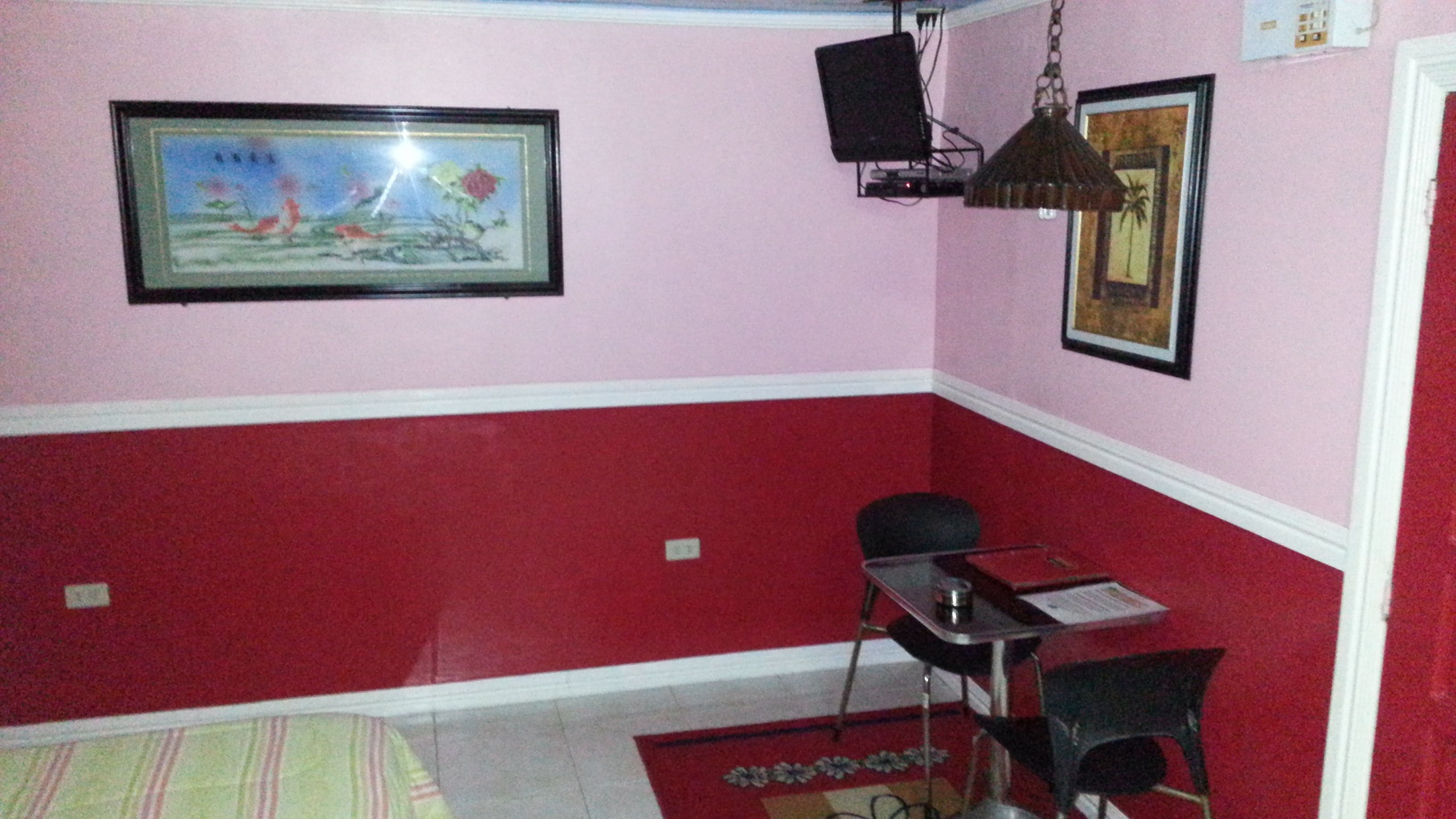 Una habitación con una decoración en tonos rojo y blanco, un escritorio con una silla, una lámpara colgante y cuadros en las paredes.