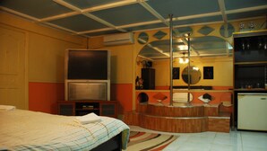 A bedroom with a bed, a TV, a mirror, and a small kitchenette. - Kokomos Hotel & Restaurant (Angeles City)