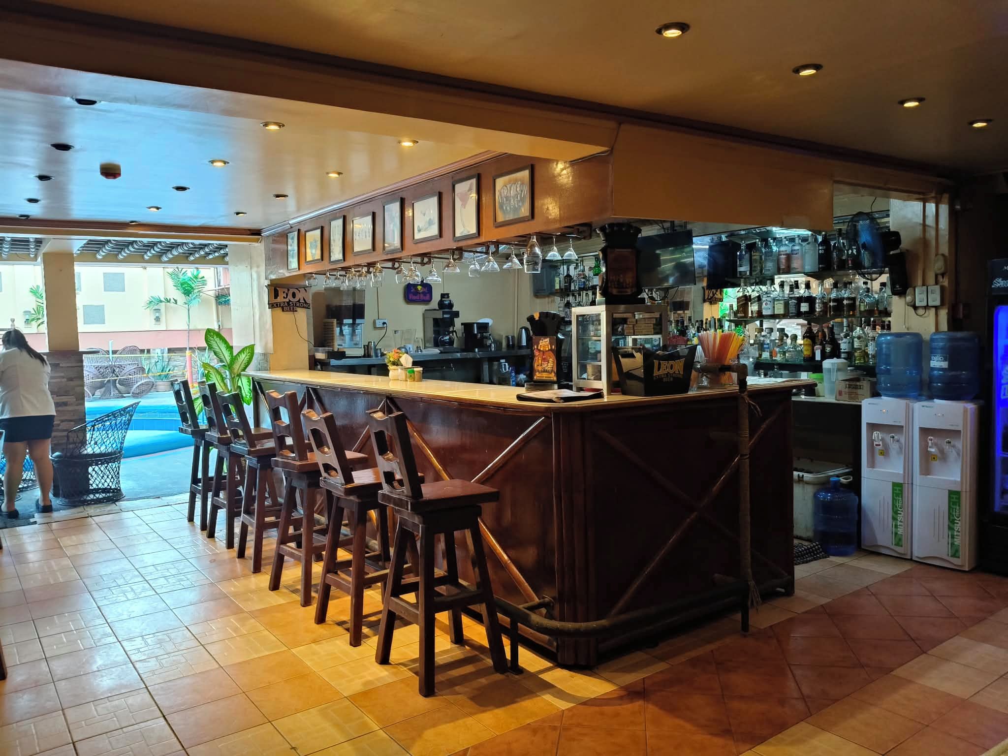 A bar area with wooden stools, a counter with a coffee machine, and a view of the outside.