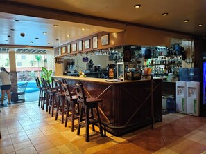A bar area with wooden stools, a counter with a coffee machine, and a view of the outside. - Kokomos Hotel & Restaurant (Angeles City)