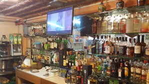 A bar with shelves stocked with various liquor bottles and a television mounted on the wall. - Kokomos Hotel & Restaurant (Angeles City)