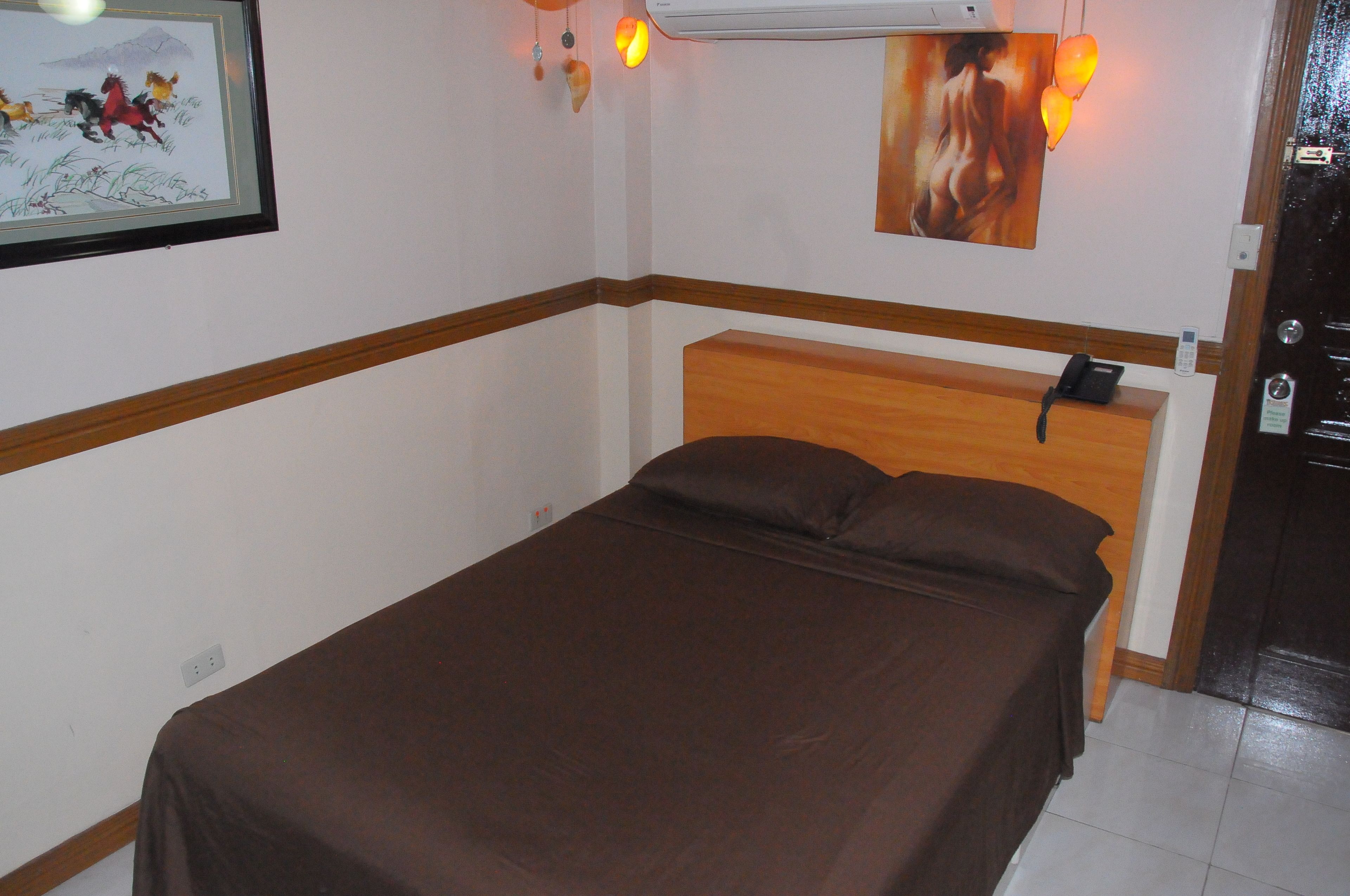 A single bed with a wooden headboard, a bedside telephone, and a wall-mounted air conditioner.