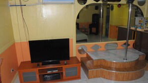 Habitación con televisión de pantalla plana sobre un soporte de madera, un espejo y una pequeña mesa con lámpara.