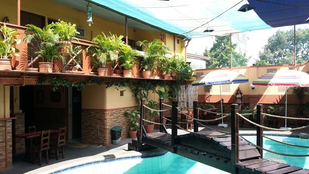 A pool area with a wooden deck, potted plants, and outdoor seating. - Kokomos Hotel & Restaurant (Angeles City)