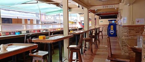 A restaurant with long communal tables, bar stools, and a counter with an ATM.