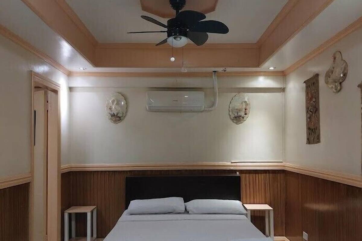 Ein Schlafzimmer mit einem Bett, einem Deckenventilator, einer Klimaanlage und einem kleinen Nachttisch.