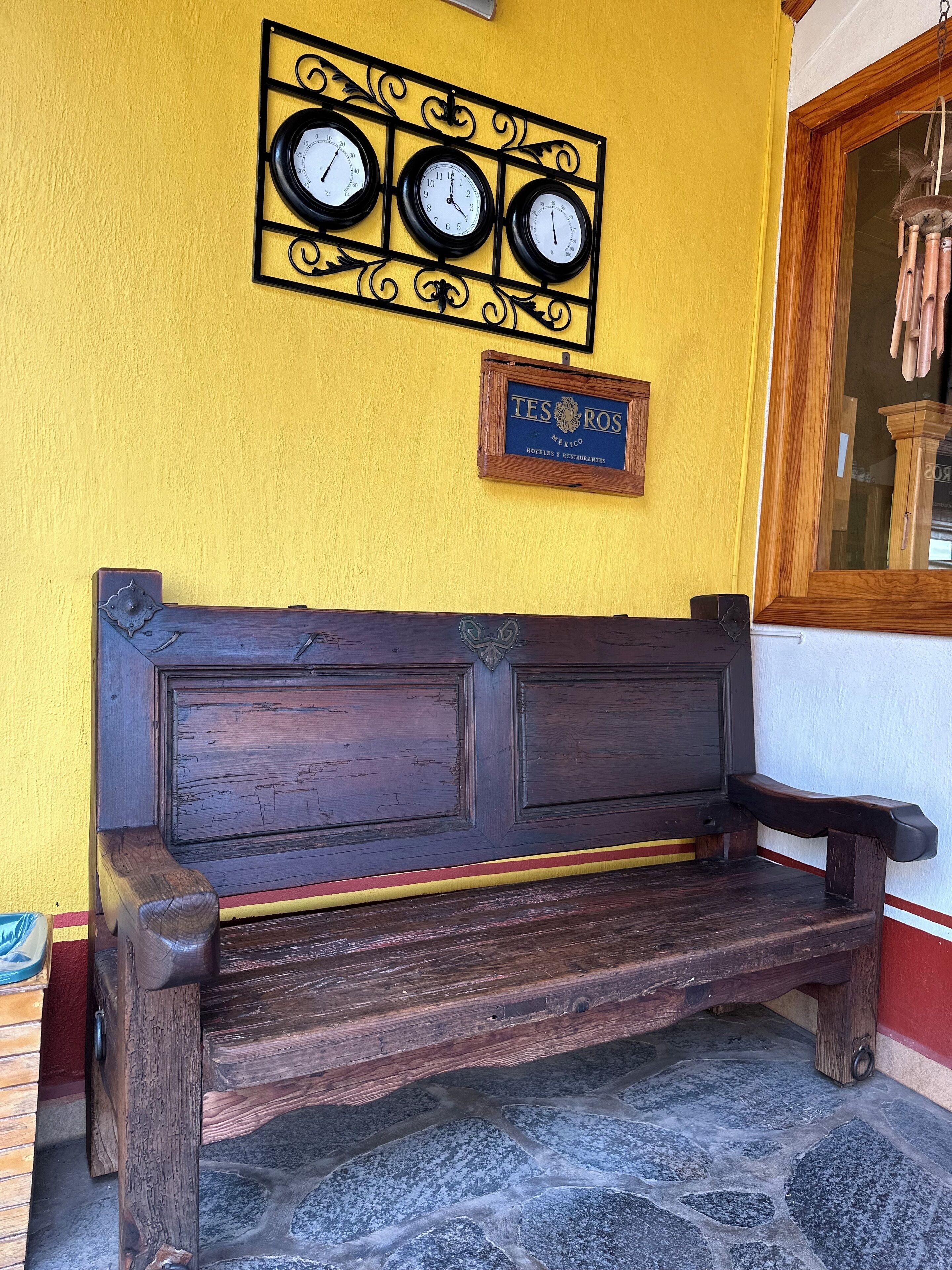 Un banco de madera con una placa que dice "TESOROS Mexico Hotels y Restaurantes" frente a una pared amarilla.