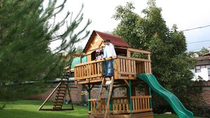 A wooden playhouse with a green slide and a ladder.