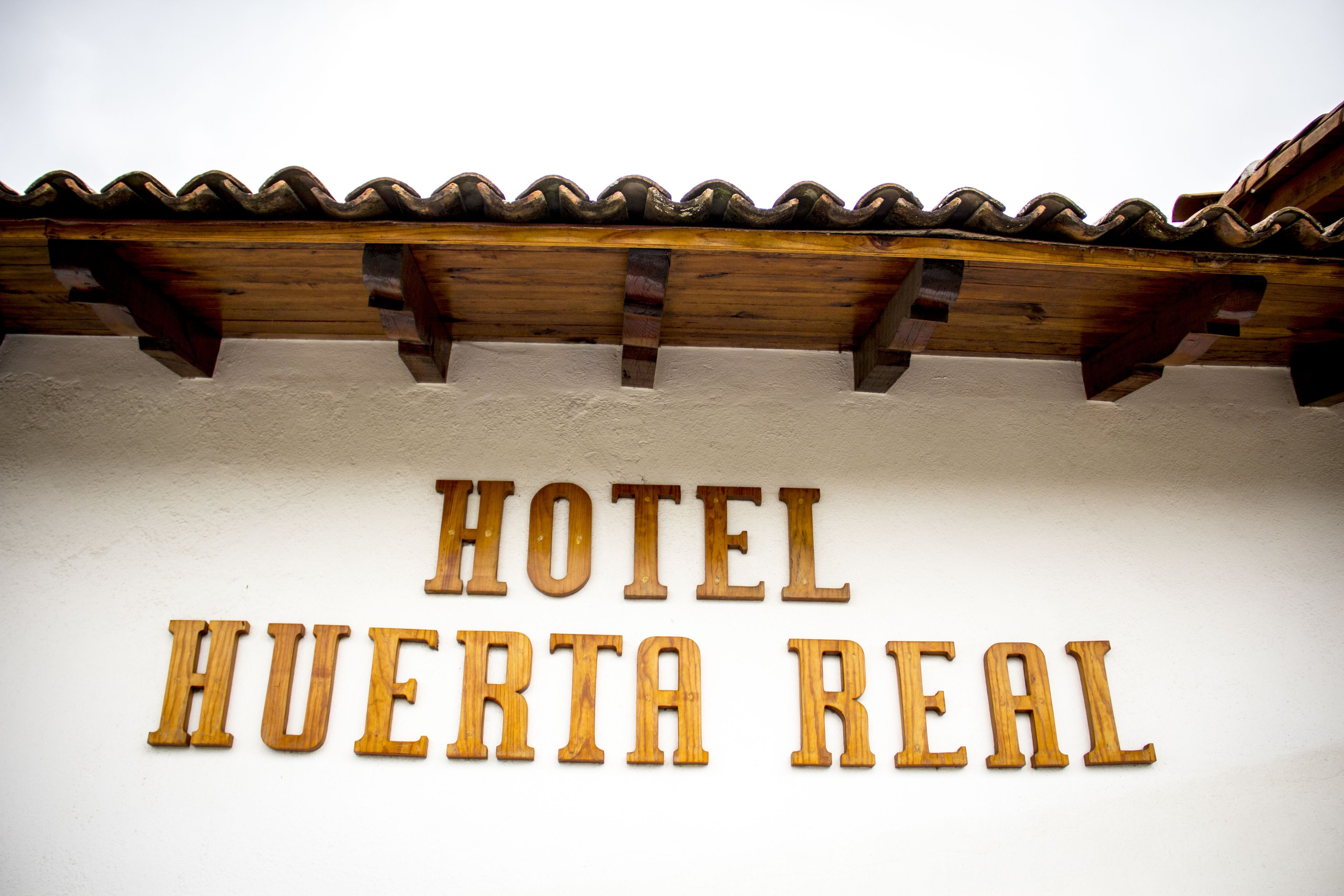 A sign with the text "HOTEL HUERTA REAL" on a white wall.