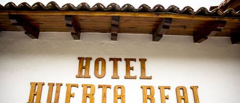 A sign with the text "HOTEL HUERTA REAL" on a white wall.