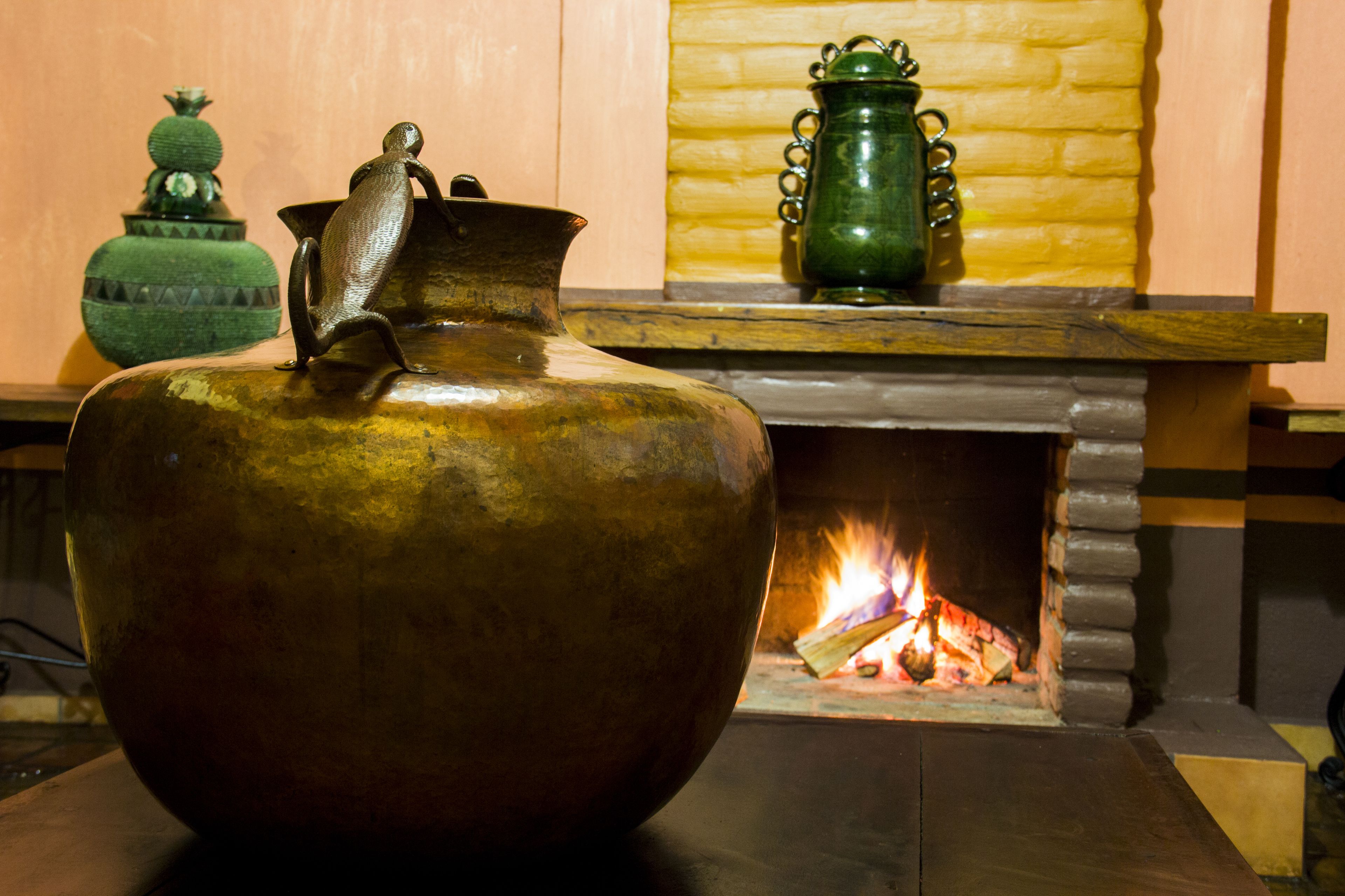 A large brass pot in front of a fireplace with a fire burning.