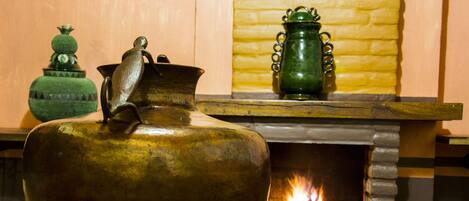 A large brass pot in front of a fireplace with a fire burning.