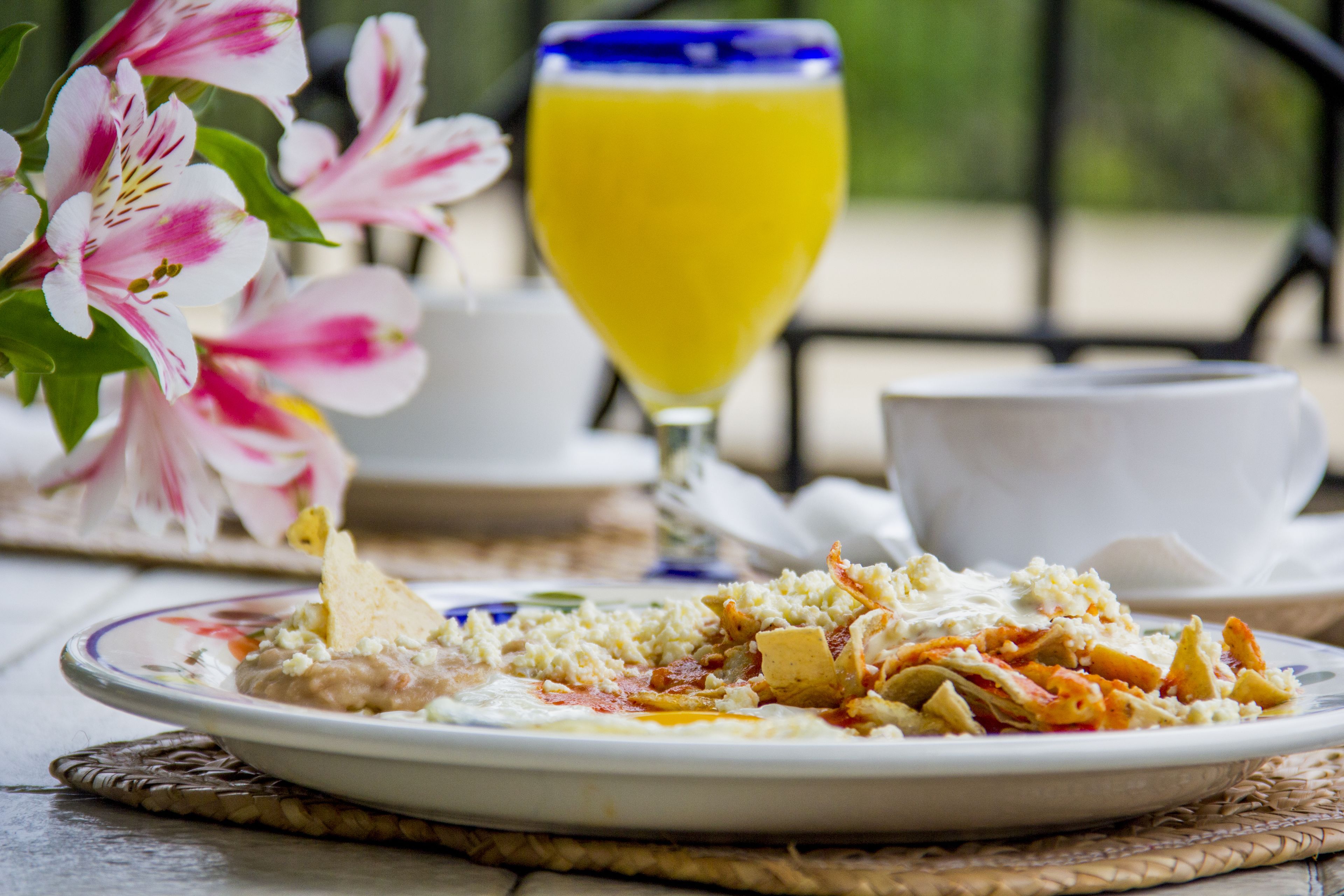 A breakfast setting with a plate of food, a glass of orange juice, and a floral arrangement.
