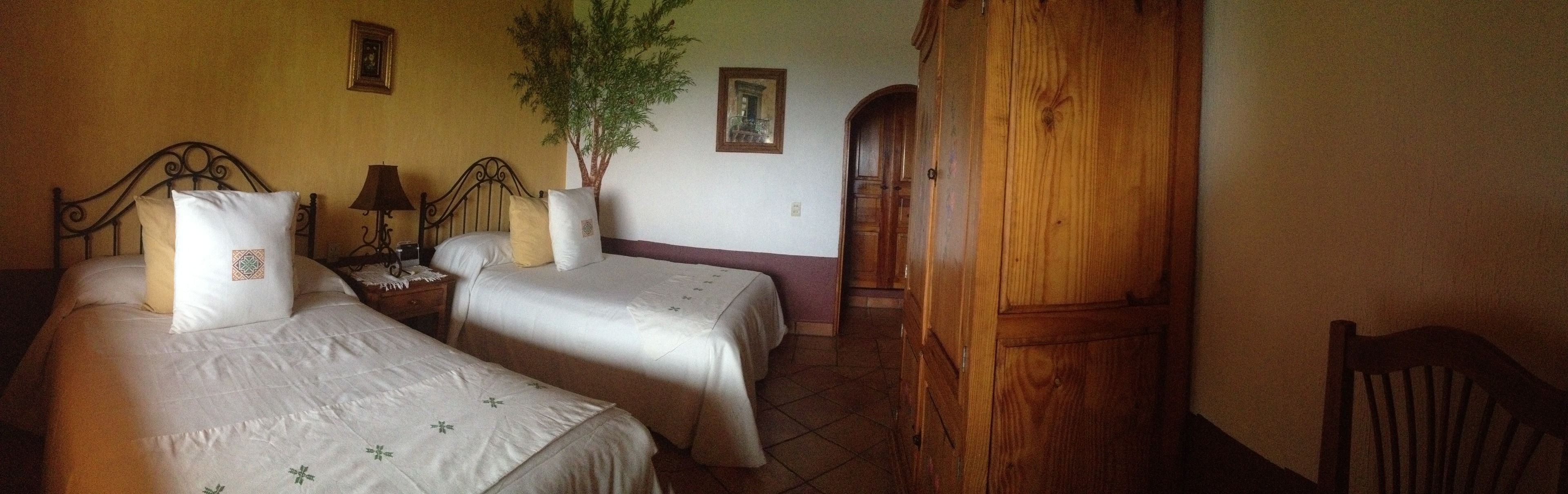 A room with two beds, a nightstand, a lamp, a potted plant, and a wooden wardrobe.