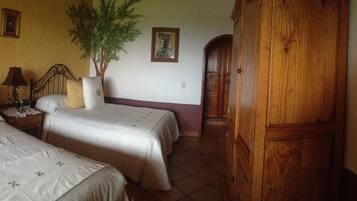 A room with two beds, a nightstand, a lamp, a potted plant, and a wooden wardrobe.