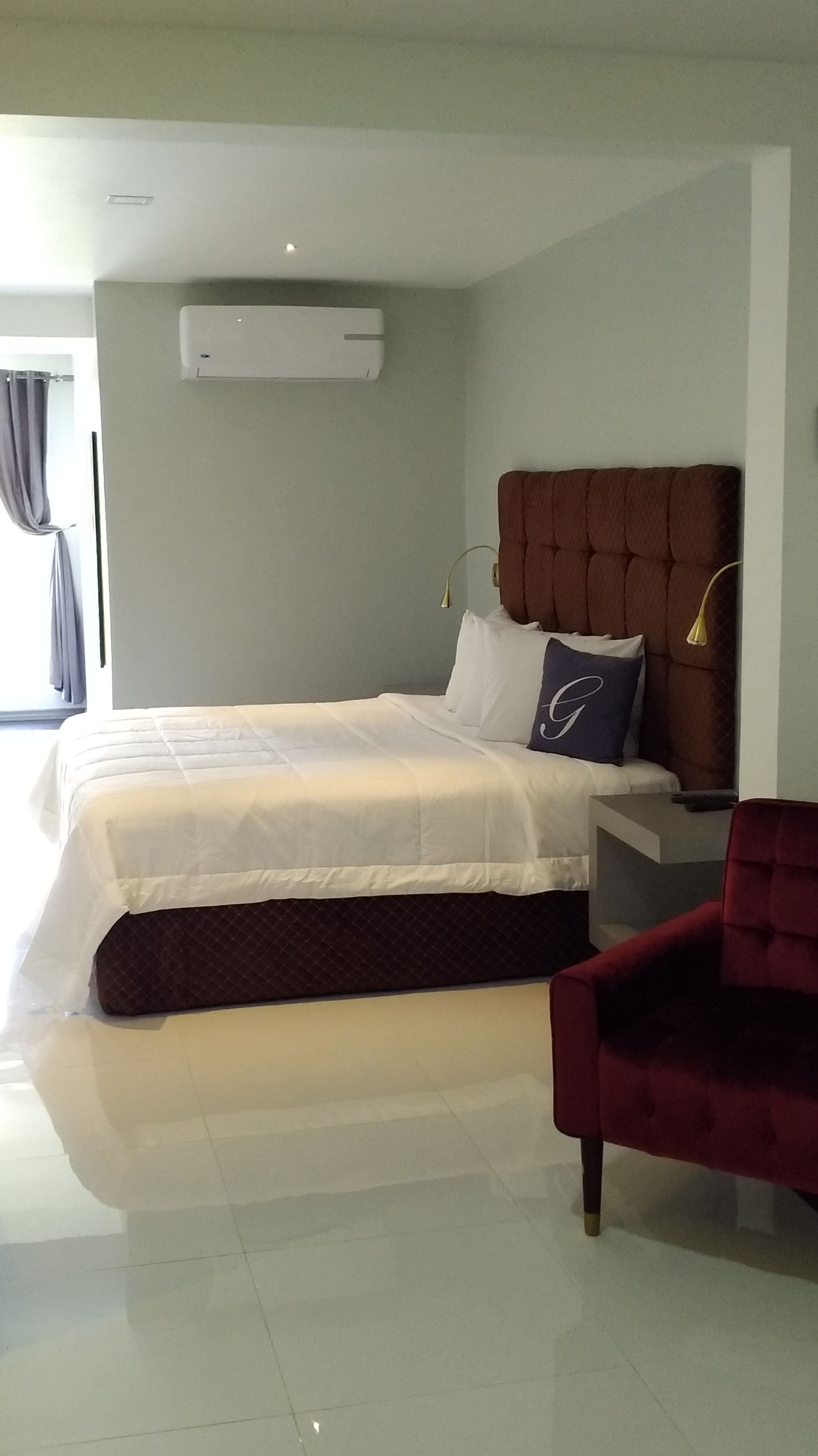A modern bedroom with a large bed, a headboard, a nightstand, and a red chair.
