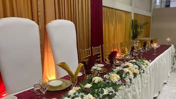 A banquet table set with white chairs, gold cutlery, and floral centerpieces.