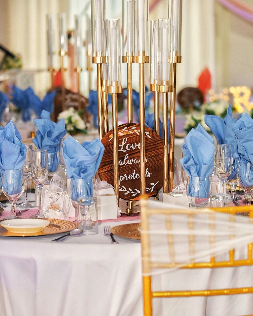 A table set with blue napkins, clear glasses, and a wooden sign with the text "Love always protects".