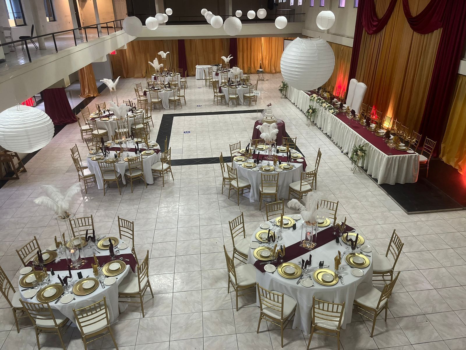 A spacious banquet hall with multiple round tables, each set with gold and white tableware, and gold chairs.