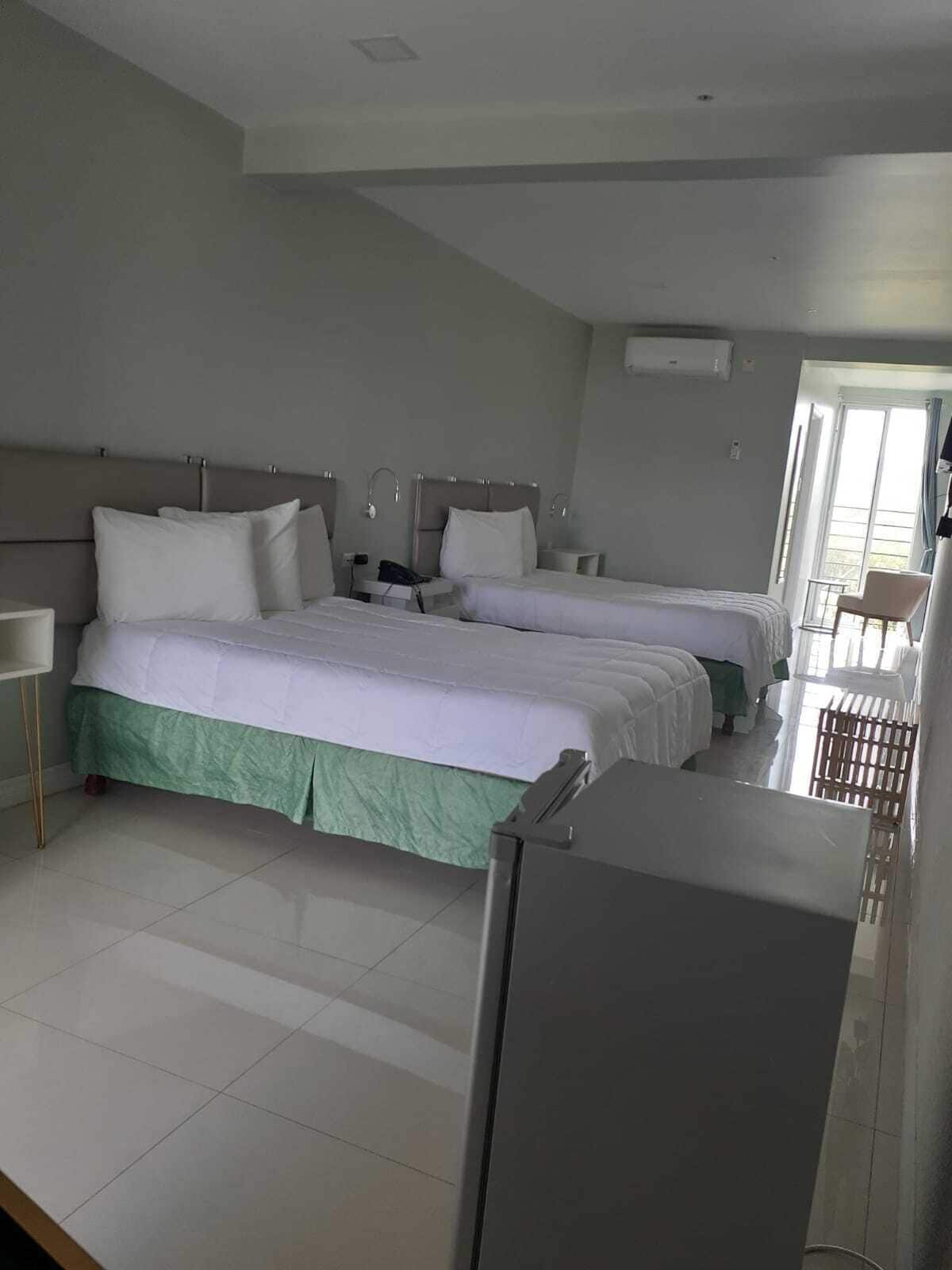 A hotel room with two beds, a small desk, a chair, and a refrigerator.
