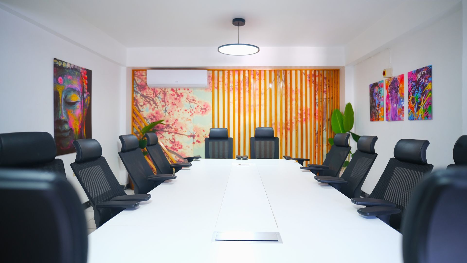 A conference room with a long table, black chairs, and colorful artwork on the walls.