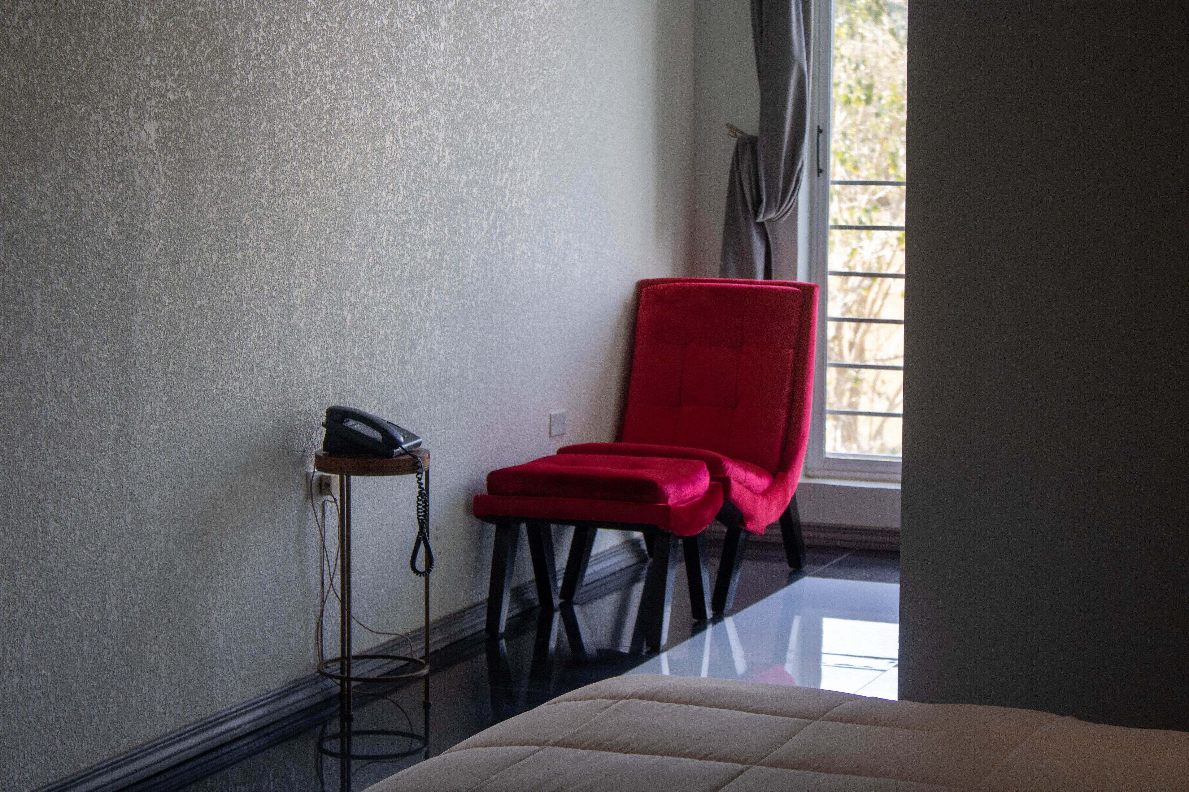 A room with a bed, a red chair, a telephone, and a window with curtains.