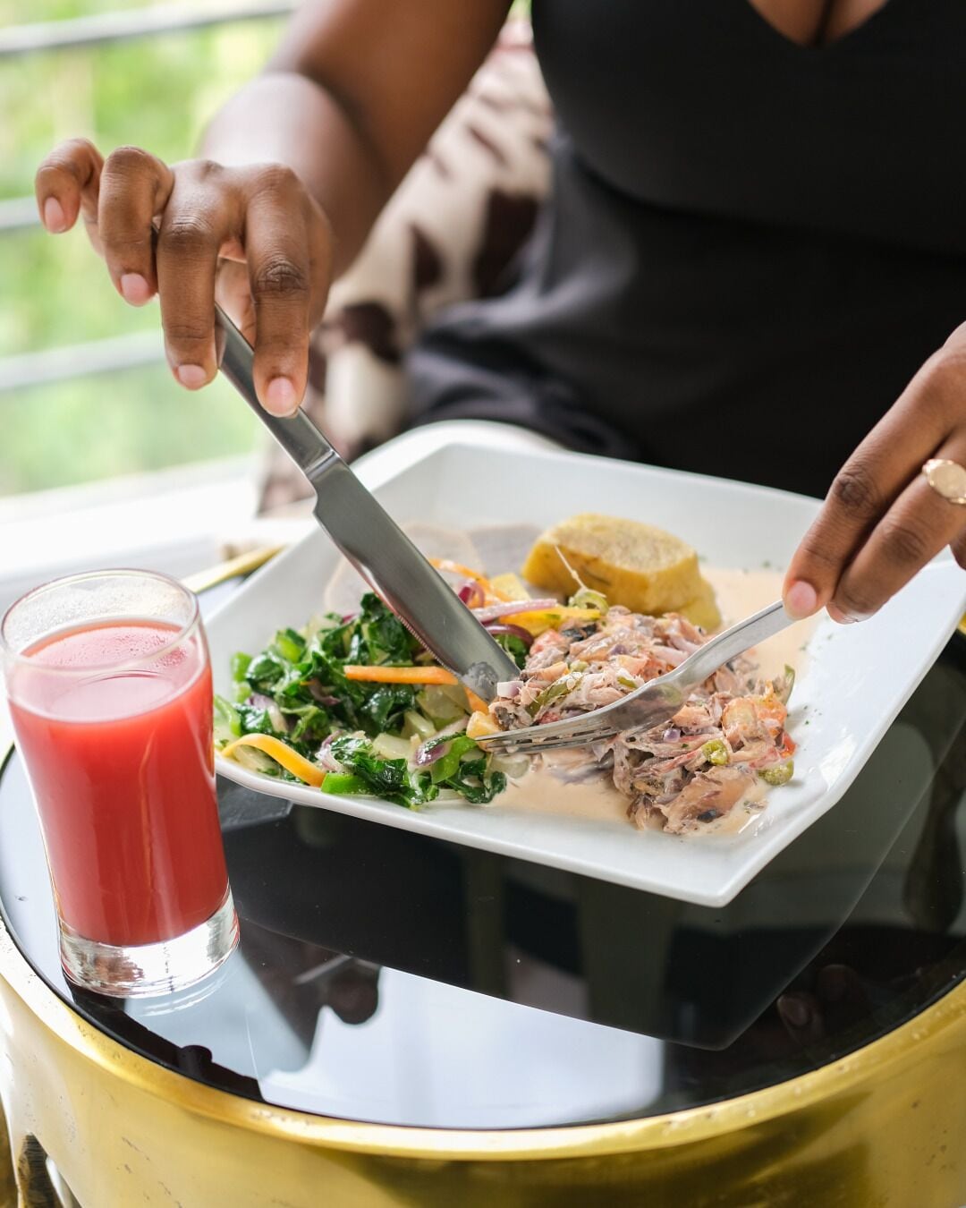 Una persona comiendo en una mesa, con un plato que incluye ensalada, un plato principal y un vaso de jugo rojo.