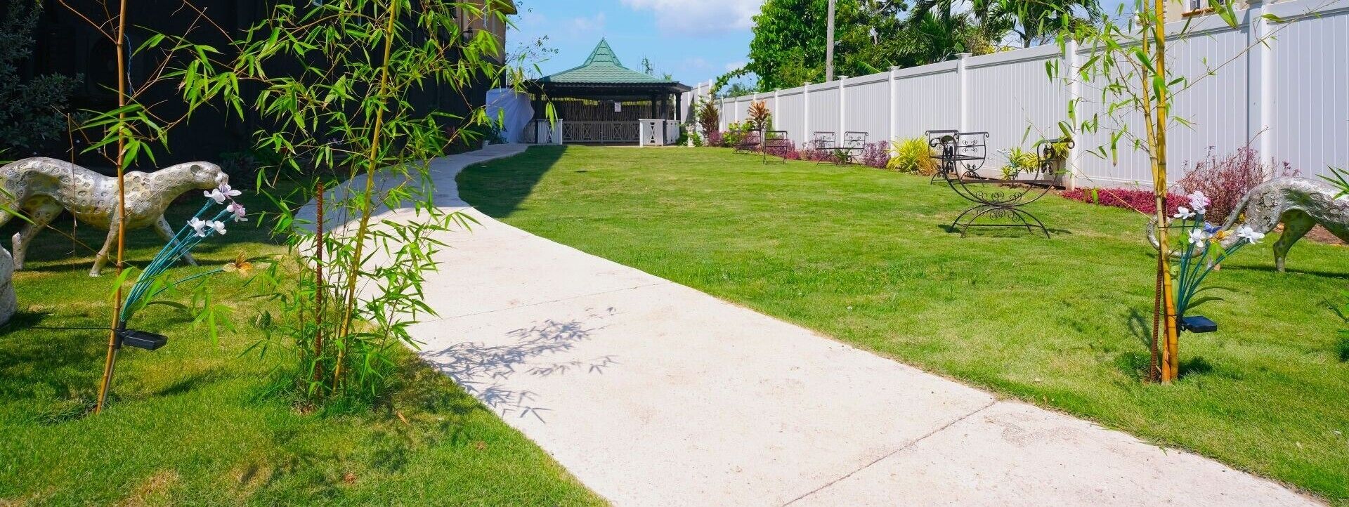 Un jardín bien cuidado con un sendero pavimentado, esculturas decorativas y un pabellón al fondo.