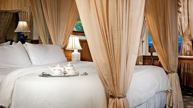 A luxurious bedroom with a large bed, a tray with teacups and a teapot, and a nightstand with a lamp. - Dorymans Oceanfront Inn (Newport Beach)