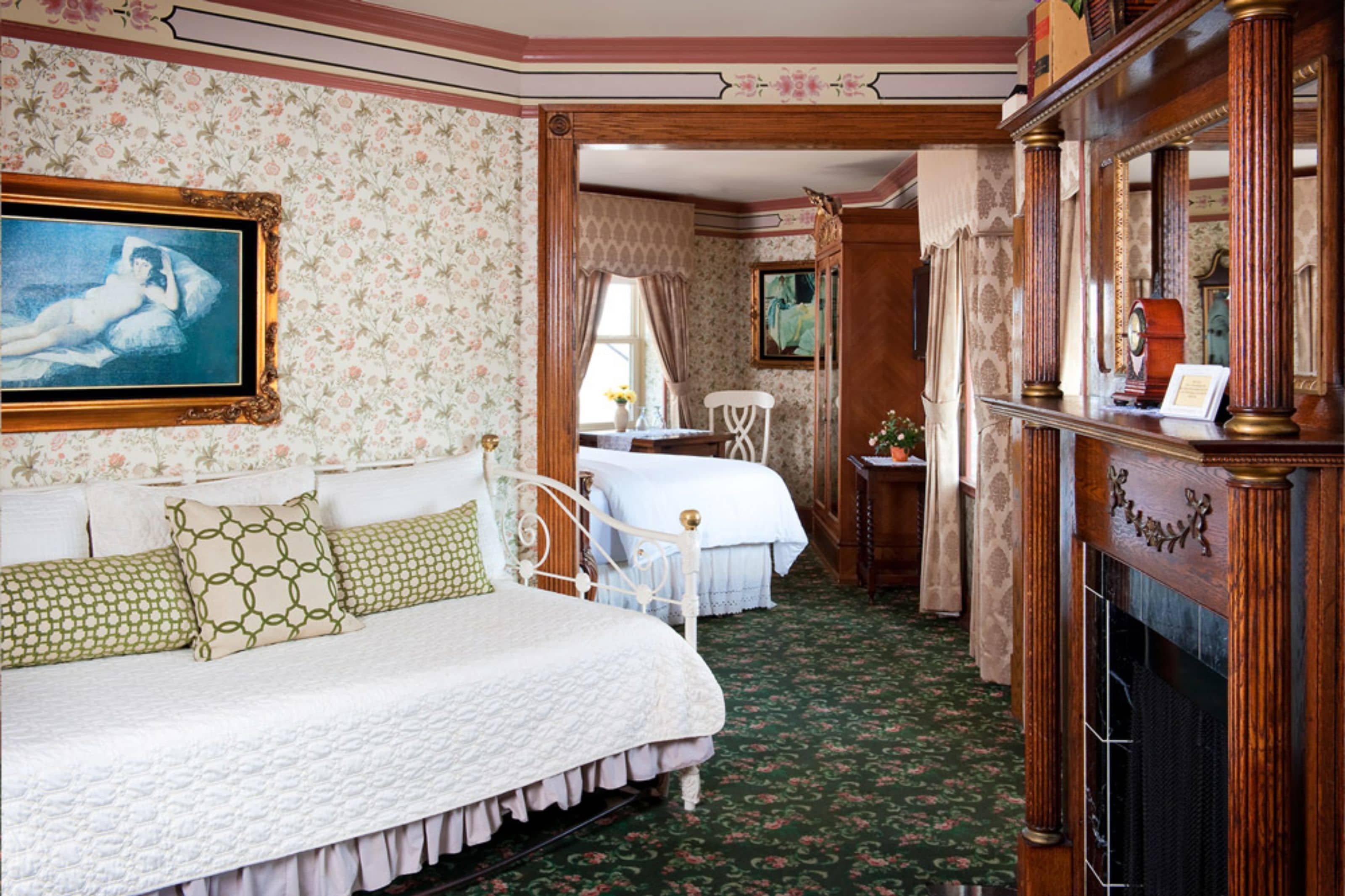 A bedroom with two beds, a fireplace, and a painting on the wall.
