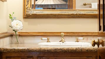 A bathroom with a marble sink, gold faucets, and a mirror with an ornate frame.
