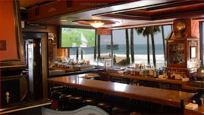 A bar with a view of the beach, bottles of alcohol, and a television screen displaying a sports game. - Dorymans Oceanfront Inn (Newport Beach)