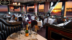 A restaurant interior with tables set for dining, a view of the ocean, and a sunset visible through the windows. - Dorymans Oceanfront Inn (Newport Beach)