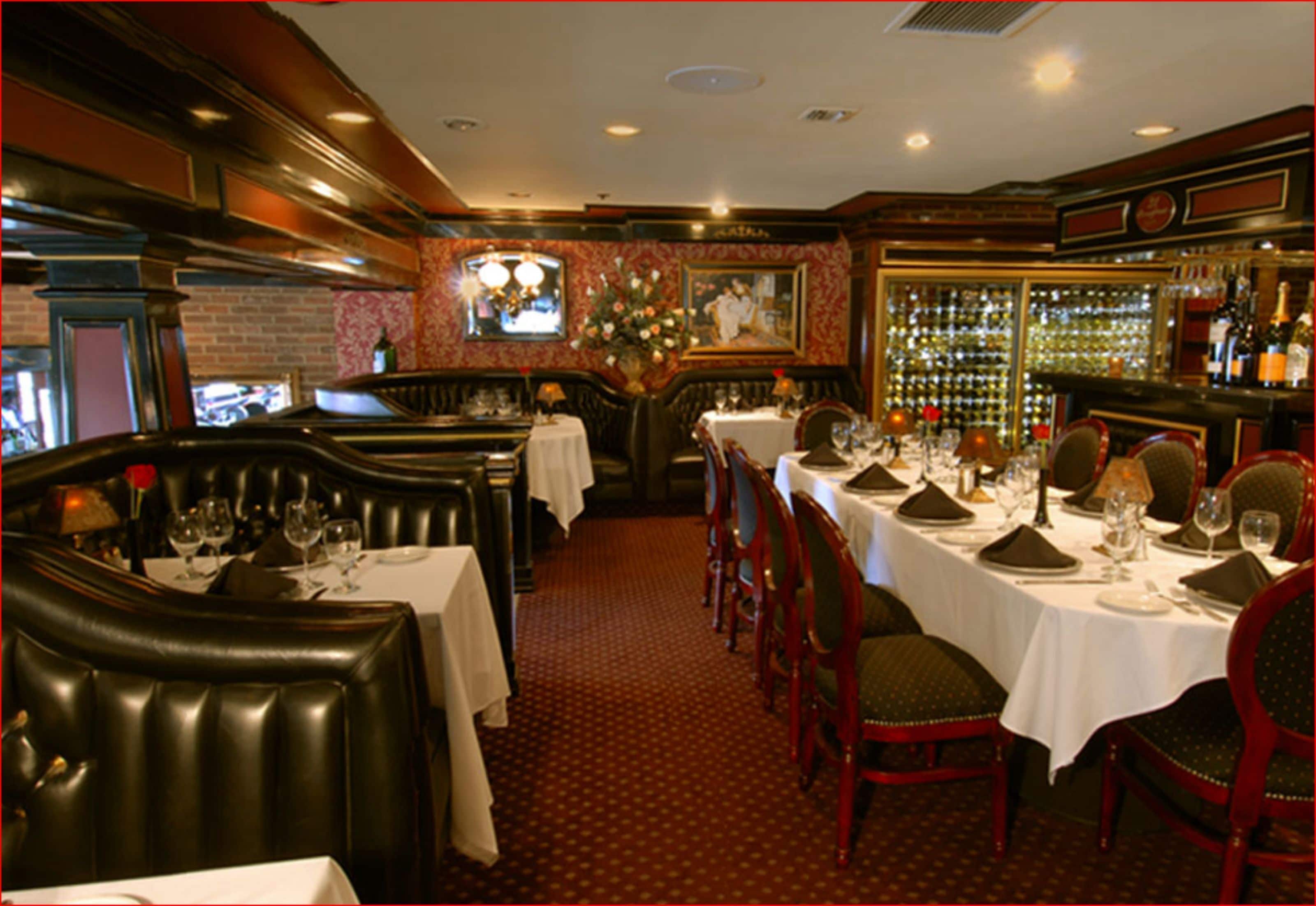 A restaurant with leather booths, white tablecloths, and red upholstered chairs.