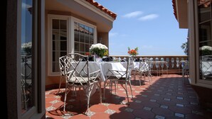 An outdoor patio with white tables and chairs, a tiled floor, and a view of the sky. - Dorymans Oceanfront Inn (Newport Beach)