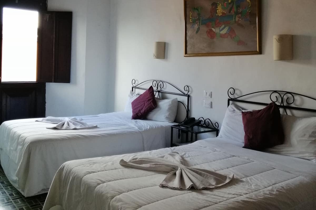 A hotel room with two beds, a ceiling fan, a painting on the wall, and a window with curtains.