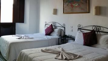 Una habitación de hotel con dos camas, un ventilador de techo, un cuadro en la pared y una ventana con cortinas.
