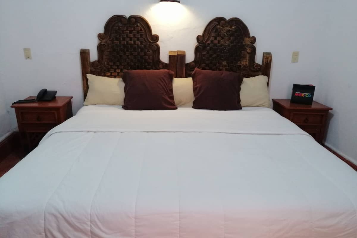 A bed with a wooden headboard, two bedside tables, and a nightstand with a phone.