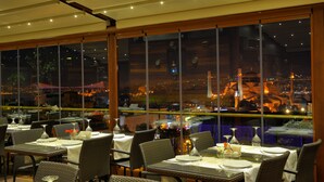 A restaurant with tables set for dining, large windows offering a view of the cityscape at night. - Burckin Hotel (Istanbul)