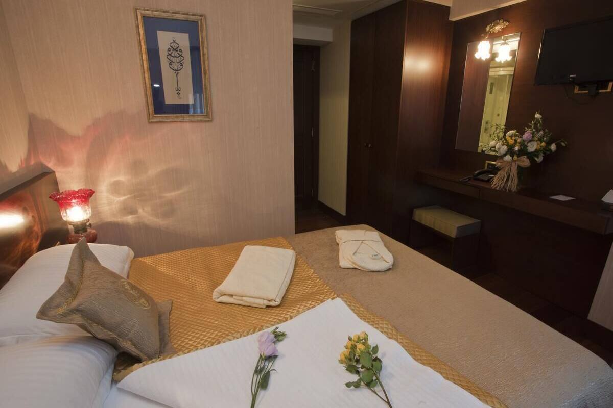A hotel room with a bed, bedside table, lamp, and a mirror with a flower arrangement.