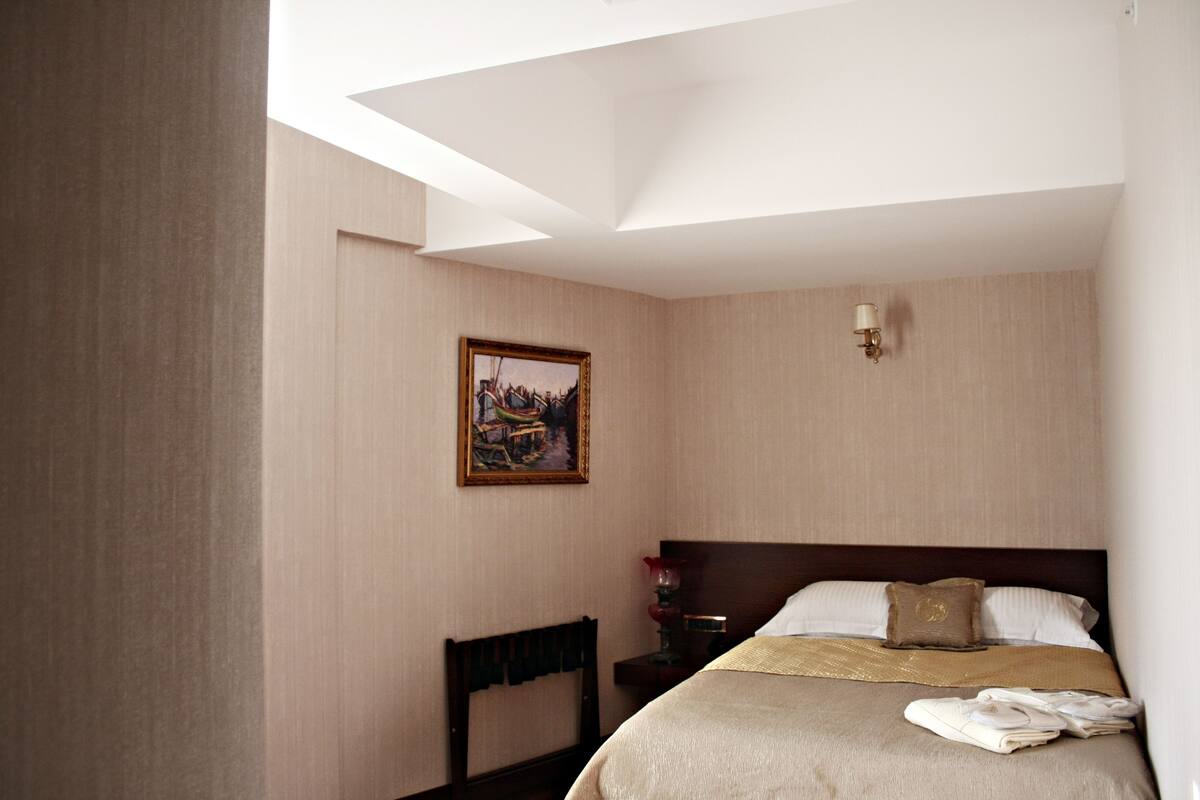 A hotel room with a bed, a nightstand, a lamp, a painting on the wall, and a chair.