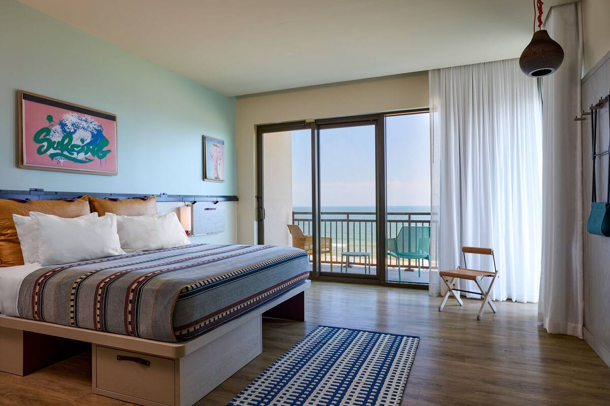 A bedroom with a large bed, a view to the outside, and a balcony with chairs.