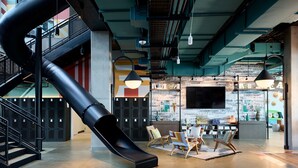 Un espacio interior moderno con un tobogán negro, suelo de madera y una zona de estar con sillas coloridas.