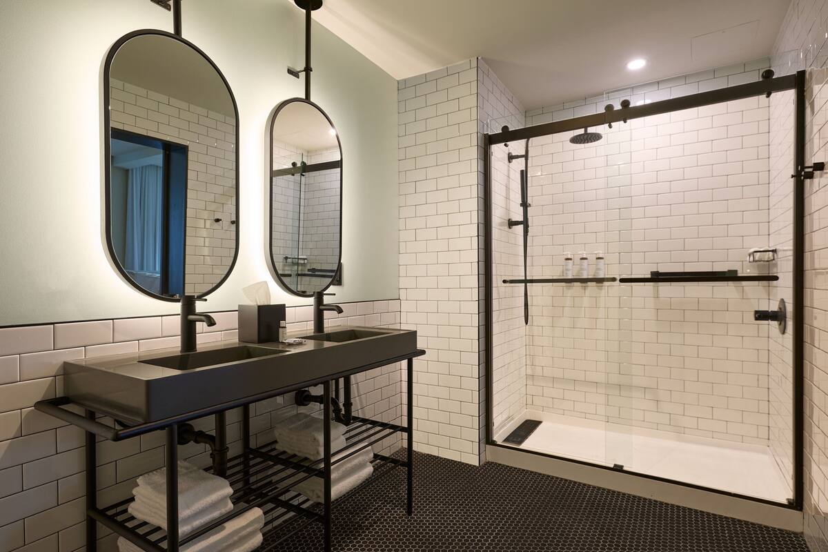 A modern bathroom with a dual sink vanity, a large mirror, and a glass-enclosed shower area.