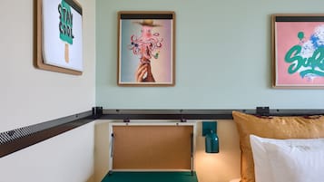 A room with a bed, a corkboard, and three framed artworks on the wall.